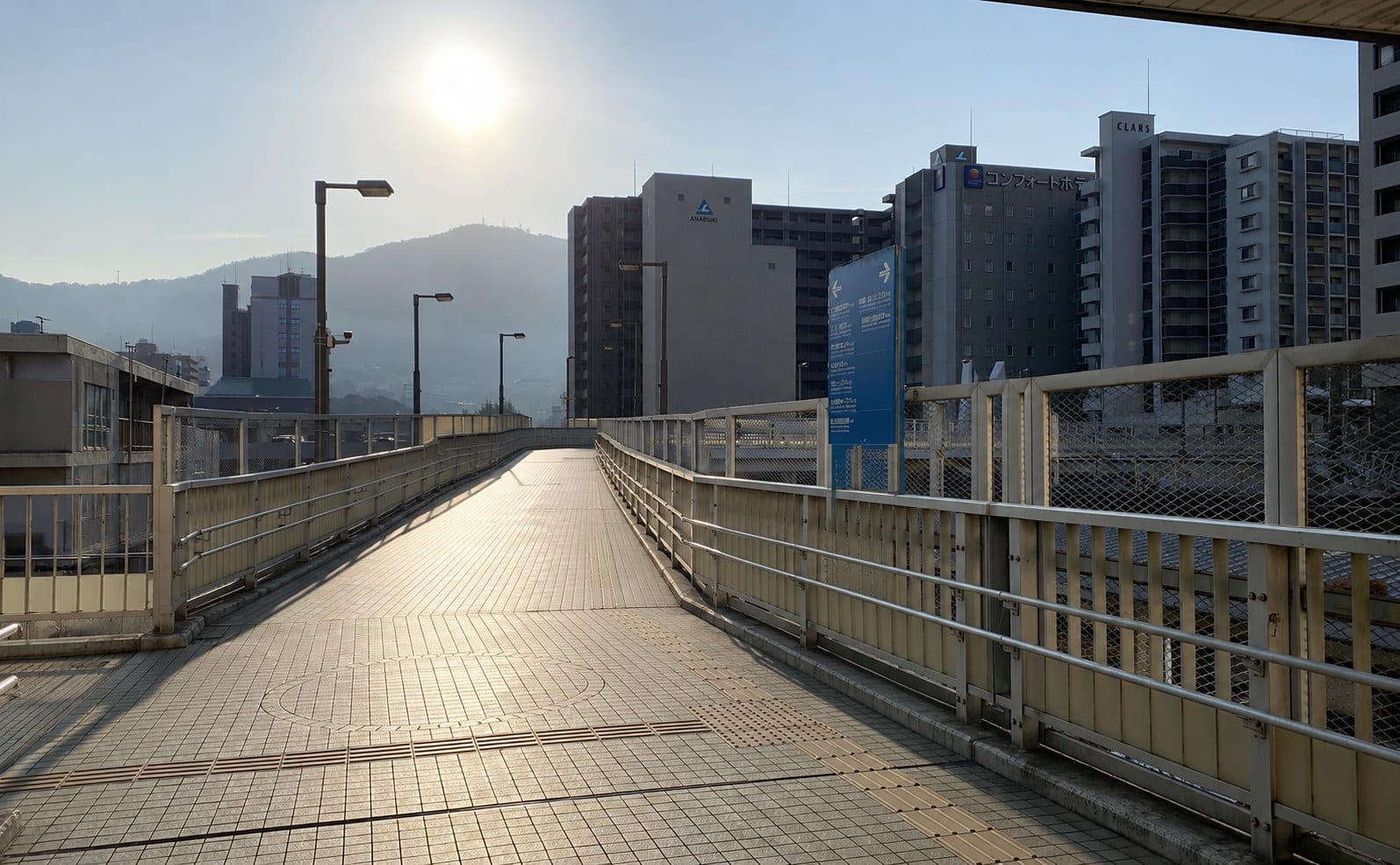 The elevated pedestrian deck leading away from Kure Station in early-morning light, with the surrounding hills visible beyond the buildings.