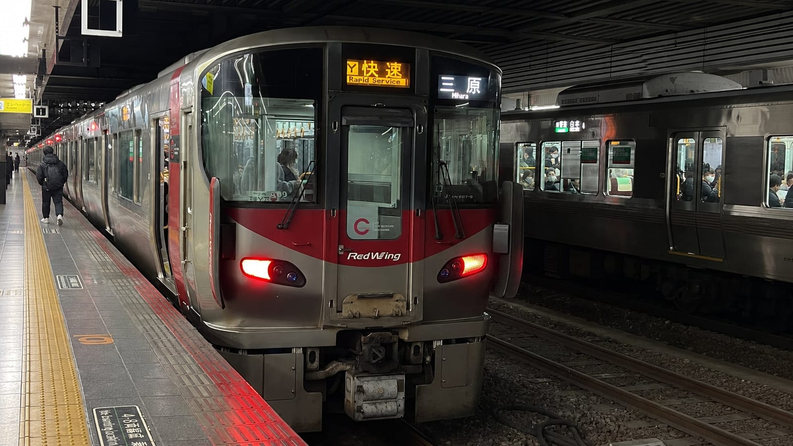 The red-and-silver 227 series "Red Wing" train at Hiroshima Station, its destination display showing a Kure Line rapid service.