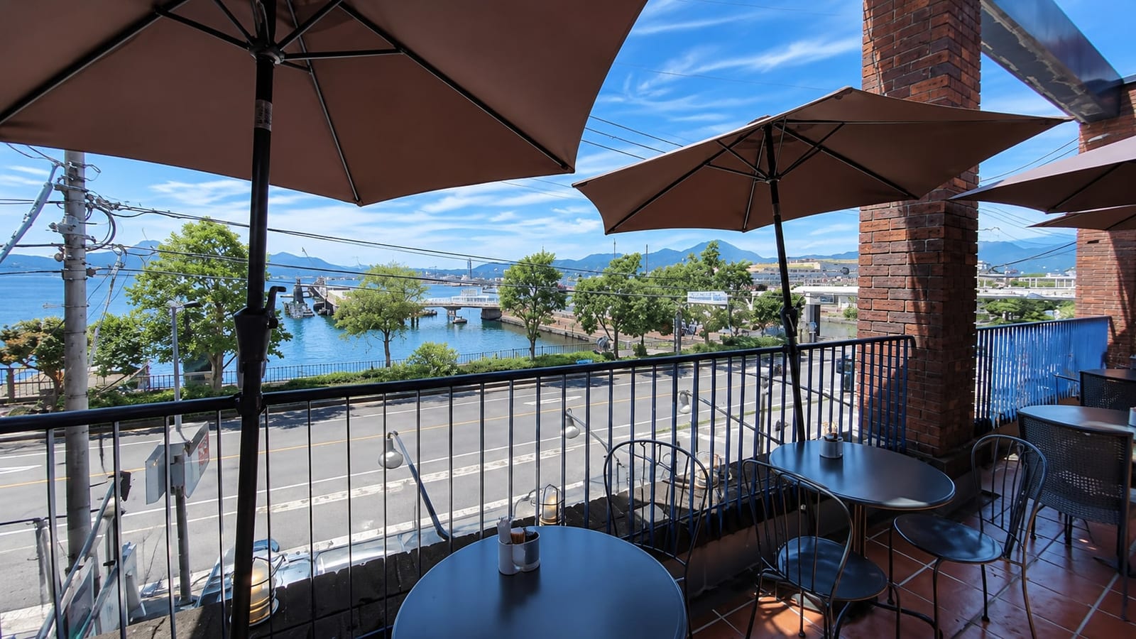 The terrace seating at Minato Machi Coffee Ten under parasols, looking across the road to the water by the JMSDF submarine pier.