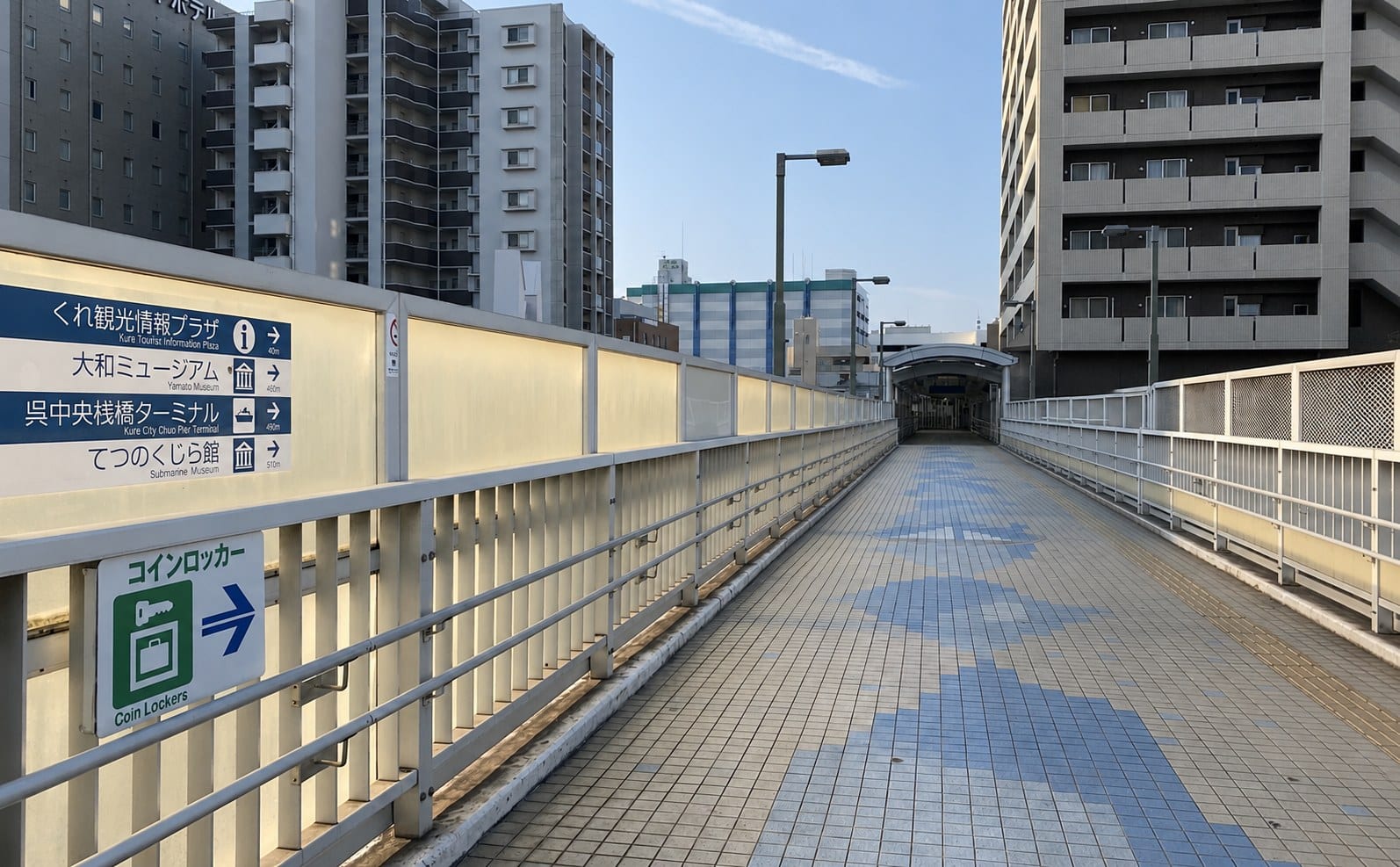 Bilingual signage on the elevated pedestrian deck outside Kure Station: Yamato Museum 460 m, Kure City Chuo Pier Terminal 490 m, Submarine Museum 510 m, with a coin-locker sign below.