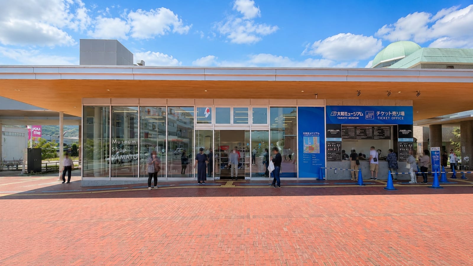 The Yamato Museum's outdoor ticket office on the brick plaza, with bilingual Japanese and English signage and a short queue at the counter windows, next to the Museum Shop Yamato.